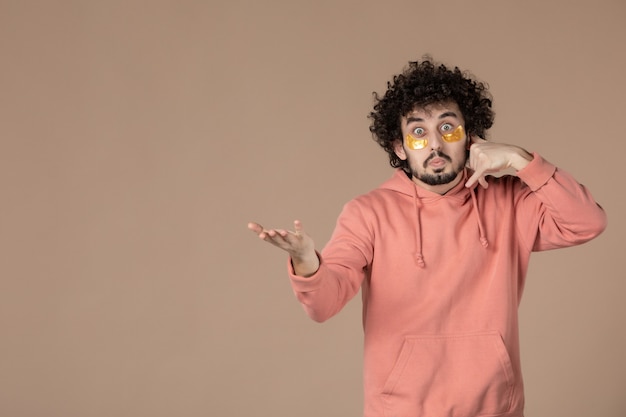 vue de face jeune homme avec des cache-œil imitant un appel téléphonique sur fond marron crème de massage peau du visage beauté soins de la peau