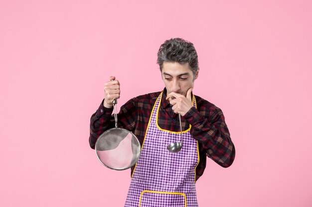 Photo vue de face jeune homme en cape avec tamis et cuillère sur fond rose cuisine cuisinier cuisine alimentaire uniforme travailleur mari horizontal