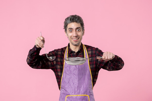 vue de face jeune homme en cape avec tamis et cuillère sur fond rose ouvrier uniforme nourriture mari cuisinier profession cuisine horizontale soupe