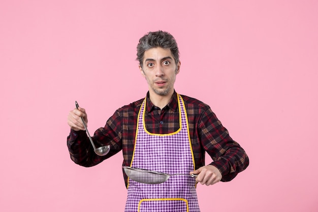Vue de face jeune homme en cape avec tamis et cuillère sur fond rose uniforme travailleur alimentaire mari cuisinier cuisine horizontale soupe profession