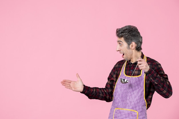 Vue de face jeune homme en cape tenant une cuillère à soupe d'argent sur fond rose profession mari cuisine cuisine cuisiner les aliments horizontale