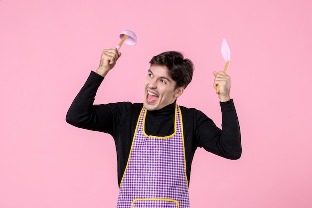 Vue de face jeune homme en cape tenant des cuillères sur fond rose profession couleur repas cuisson cuisine horizontale travail nourriture pâte uniforme