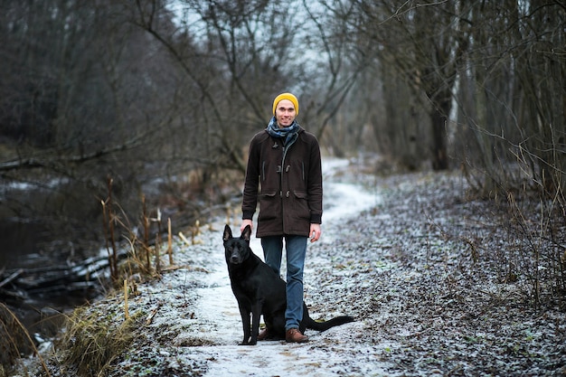 Vue de face à un jeune homme caucasien élégant formation avec gros chien noir en plein air