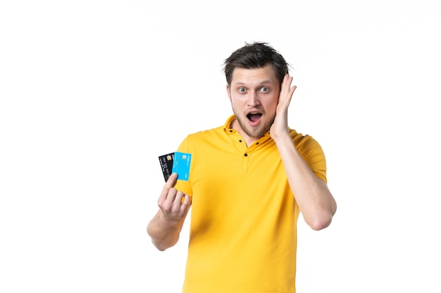 Vue de face jeune homme en chemise jaune tenant une paire de cartes bancaires sur fond blanc emploi uniforme dépenser de l'argent couleur travailleur humain