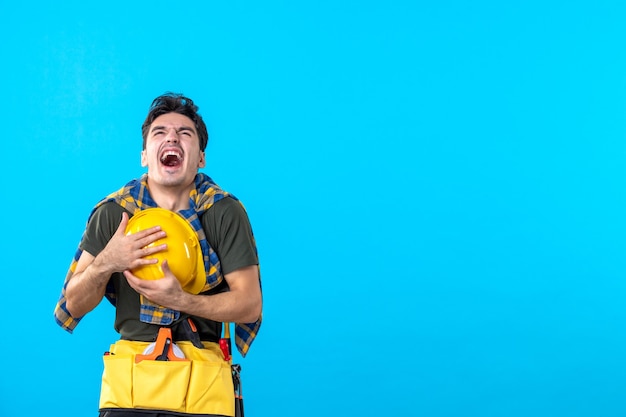 Vue de face jeune homme constructeur avec casque jaune sur fond bleu architecture constructeur maison outil de construction travailleur plat