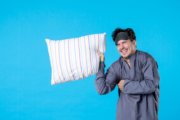 Vue de face jeune homme dans son pyjama tenant un oreiller sur fond bleu couleur cauchemar humain reste rêve nuit sommeil lit réveil