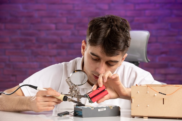 Vue De Face Jeune Homme Derrière Le Bureau Essayant De Réparer Peu De Mise En Page Sur Le Mur Violet