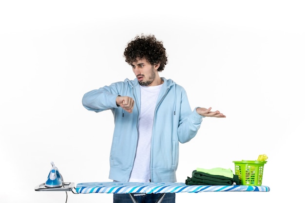 vue de face jeune homme derrière une planche à repasser contrôle de l'heure sur fond blanc ménage couleur blanchisserie nettoyage des vêtements fer à repasser photo