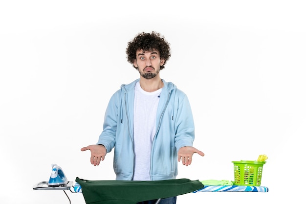 Vue de face jeune homme derrière une planche à repasser sur fond blanc émotion des tâches ménagères couleur fer à repasser les vêtements de nettoyage de blanchisserie