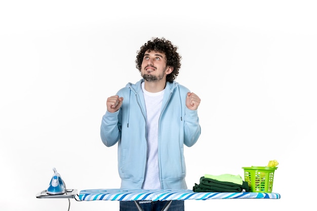 Vue de face jeune homme derrière une planche à repasser se réjouir sur fond blanc les travaux ménagers blanchisserie couleur nettoyage des vêtements fer à repasser photo