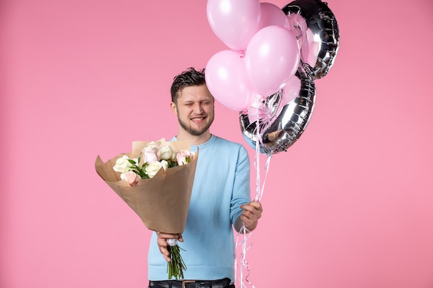 Photo vue de face jeune homme avec des fleurs et des ballons en mars présent sur fond rose amour horizontal féminin journée des femmes sensuelle date égalité