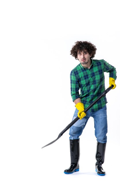 Vue de face jeune homme jardinier imitant creuser avec une pelle sur fond blanc arbre d'emploi champ de fleurs de l'herbe uniforme de l'eau