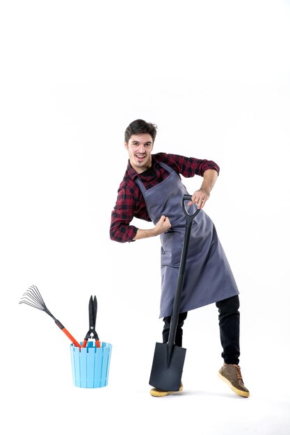 Vue de face jeune homme jardinier avec pelle noire sur fond blanc jardin creusant travail uniforme travail au sol fleur du sol