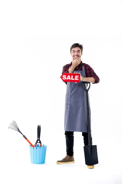 Vue de face jeune homme jardinier avec pelle noire et vente écrit sur fond blanc travail argent jardin creuser fleur de sol uniforme