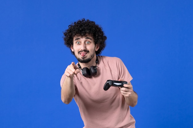 vue de face jeune homme jouant à un jeu vidéo avec manette de jeu noire sur fond bleu canapé virtuel jeunesse joueur de football gagnant joie teen