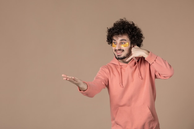 vue de face jeune homme avec des patchs oculaires imitant un appel téléphonique sur fond marron crème de massage soin du visage de la peau spa beauté couleurs