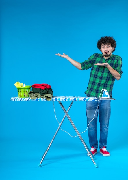 vue de face jeune homme avec planche à repasser sur fond bleu machine à laver maison vêtements de ménage couleur propre