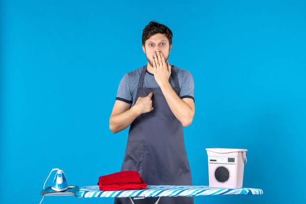 Photo vue de face jeune homme avec planche à repasser sur fond bleu ménage fer blanchisserie nettoyage machine à laver homme couleur