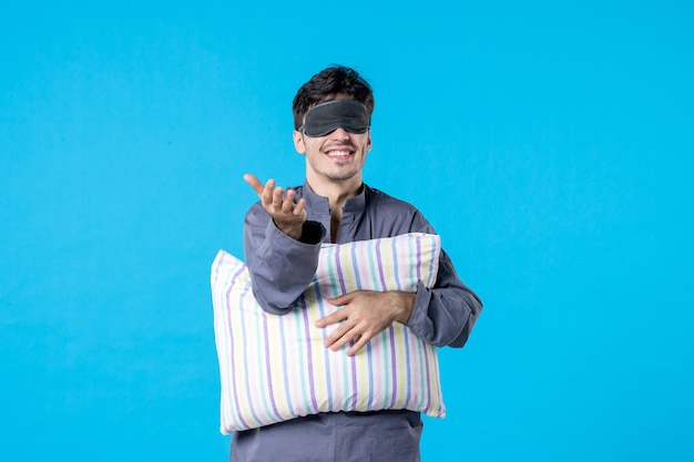 vue de face jeune homme en pyjama et bandage pour dormir tenant un oreiller sur fond bleu couleur cauchemar tardif nuit humaine réveil sommeil lit de rêve