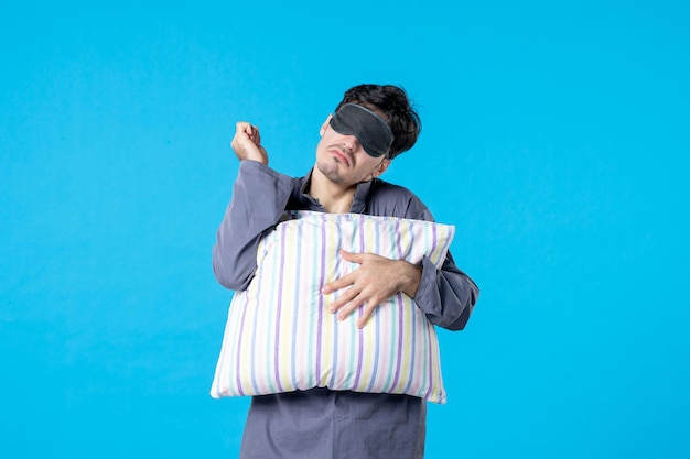 vue de face jeune homme en pyjama et bandage pour dormir tenant un oreiller sur fond bleu couleur cauchemar tardif repos de nuit humain réveil sommeil lit de rêve