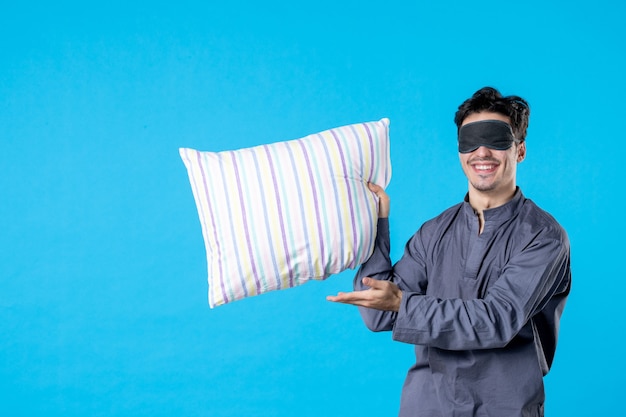 vue de face jeune homme en pyjama et bandage pour dormir tenant un oreiller sur fond bleu couleur reste cauchemar rêve sommeil tardif lit réveil nuits humaines