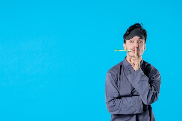 vue de face jeune homme en pyjama avec brosse à dents dans sa bouche sur fond bleu nuit couleur rêve oreiller cauchemar réveil repos lit humain sombre calme