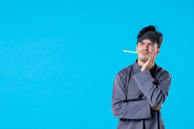 vue de face jeune homme en pyjama avec brosse à dents dans sa bouche sur fond bleu nuit de repos couleur rêve cauchemar réveil lit oreiller humain