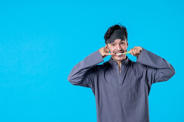 Vue de face jeune homme en pyjama nettoyer ses dents sur fond bleu couleur reste nuit réveil lit oreiller sombre cauchemar humain