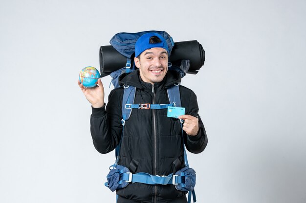 vue de face jeune homme avec sac à dos tenant un globe terrestre et une carte bancaire sur fond blanc campagne de montagne air argent forêt nature camp froid