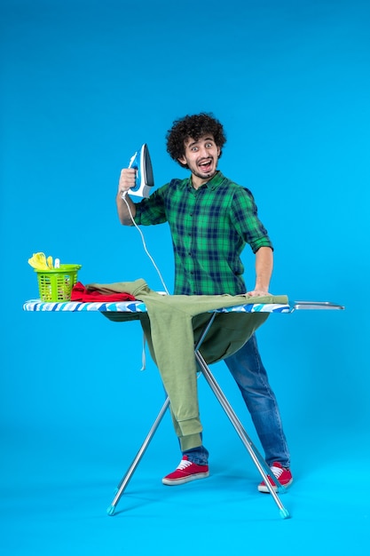 vue de face jeune homme se préparant à repasser chemise verte sur fond bleu machine à laver propre couleur de la maison humaine