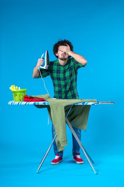 vue de face jeune homme se préparant à repasser le maillot vert sur fond bleu machine à laver propre travaux ménagers couleur humaine