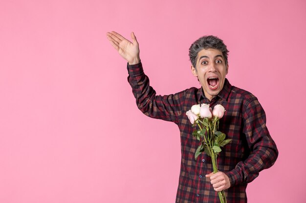 Vue de face jeune homme tenant de belles roses roses sur un mur rose