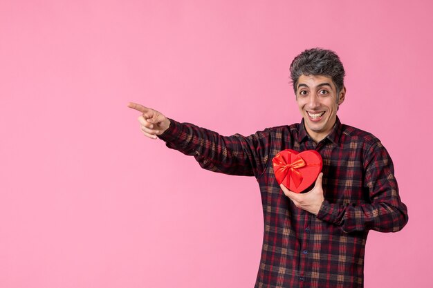 Vue De Face Jeune Homme Tenant Un Cadeau En Forme De Coeur Rouge Sur Un Mur Rose