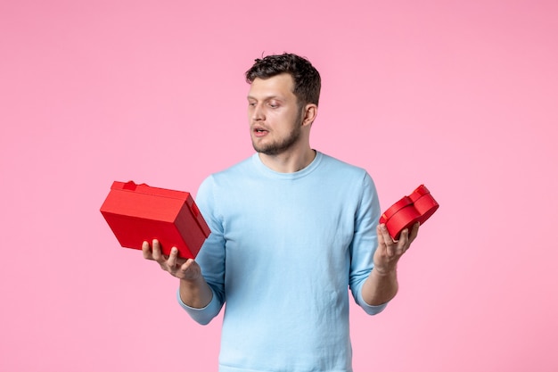vue de face jeune homme tenant des cadeaux dans des paquets rouges sur fond rose date d'amour mariage féminin sensuel journée des femmes mars égalité horizontale