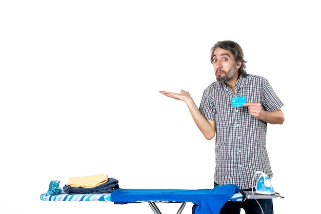 Vue de face jeune homme tenant une carte bancaire derrière une planche à repasser sur fond blanc blanchisserie fer à repasser argent vêtements machine accueil