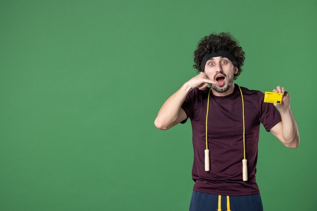 vue de face jeune homme tenant une carte bancaire jaune sur fond vert style de vie entraînement sport athlète argent santé couleur