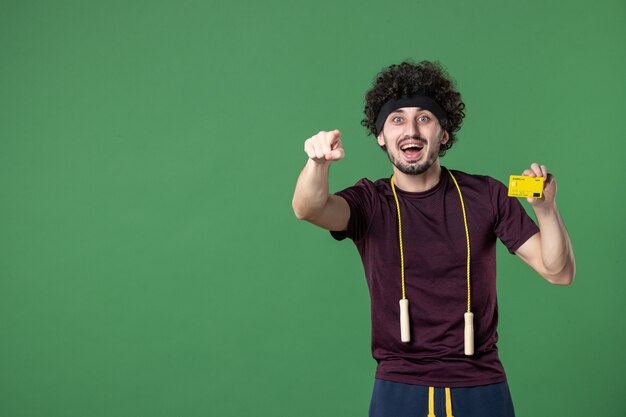 vue de face jeune homme tenant une carte bancaire jaune sur fond vert style de vie entraînement sport athlète santé salle de sport couleur