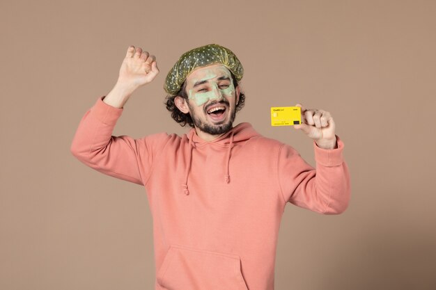 vue de face jeune homme tenant une carte de crédit jaune sur fond marron peau salon thérapie soins de la peau soins du corps spa argent