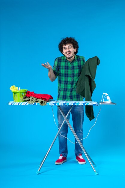 vue de face jeune homme tenant une chemise verte sur fond bleu machine à laver propre travaux ménagers couleur de la maison humaine