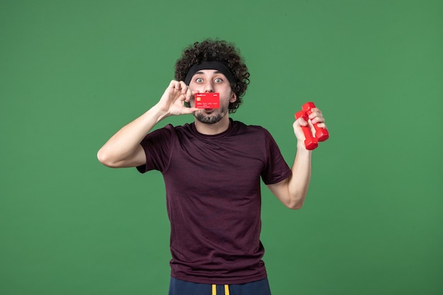 vue de face jeune homme tenant des haltères et une carte bancaire sur fond vert athlète entraînement sport gym modèle santé shopping