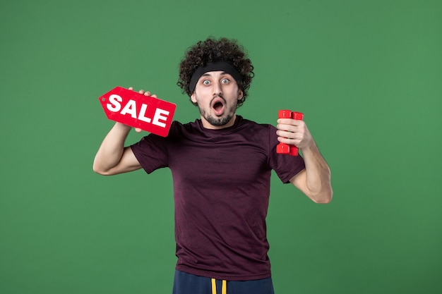 Vue de face jeune homme tenant des haltères et vente écrit sur fond vert sport gym santé athlète mode de vie modèle de couleur