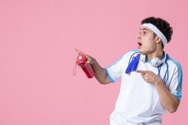 Photo vue de face jeune homme en vêtements de sport avec corde à sauter et mur rose de l'eau