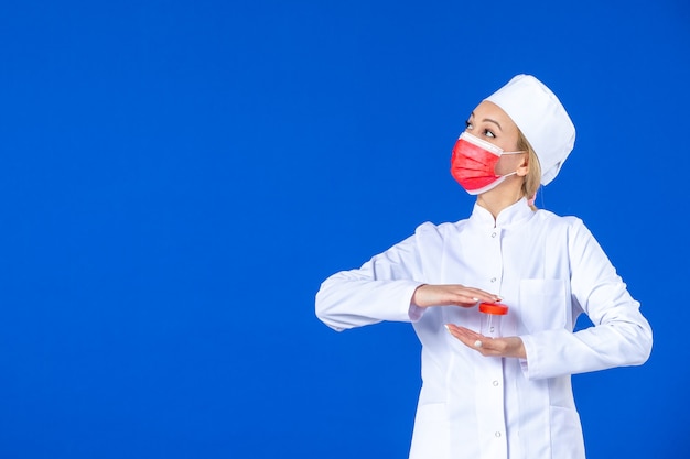 vue de face jeune infirmière en combinaison médicale avec masque tenant une fiole sur fond bleu virus de la drogue covid- médecine vaccin hôpital pandémie santé