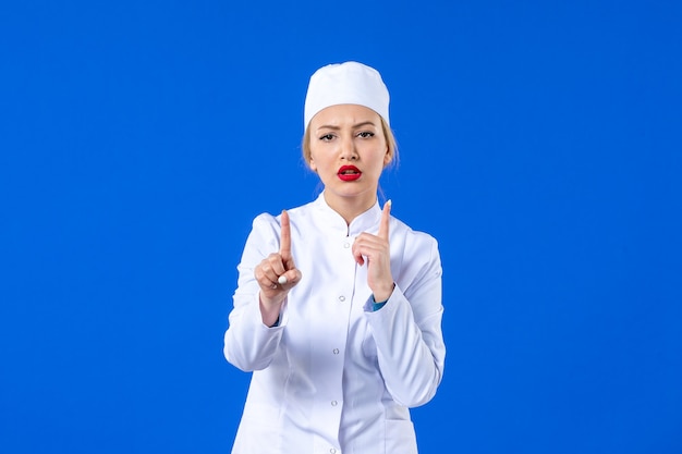 vue de face d'une jeune infirmière en costume médical blanc sur un mur bleu