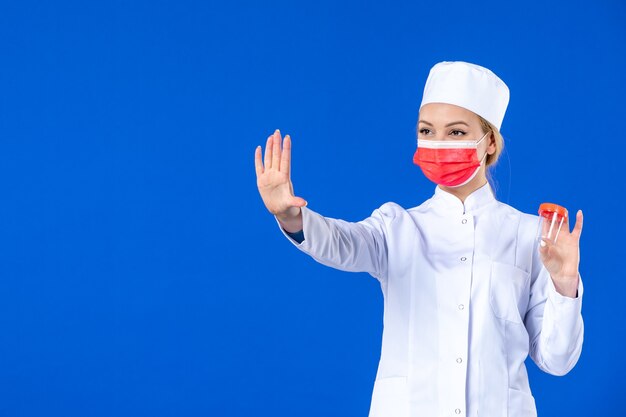 vue de face jeune infirmière en costume médical avec masque tenant une fiole sur fond bleu pandémie covid- médecine hospitalière médecin santé médicaments virus vaccin