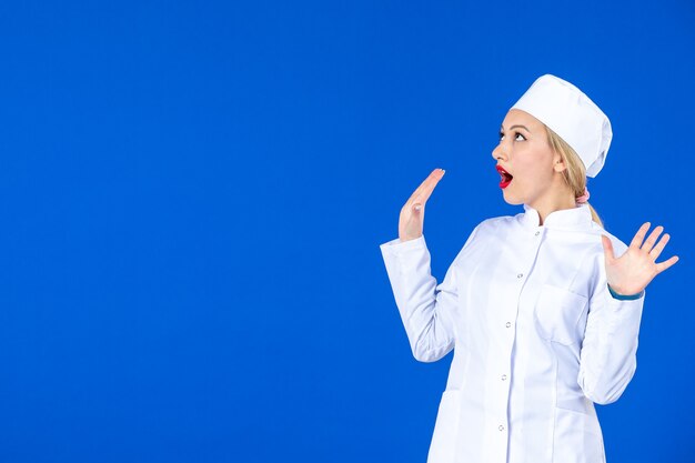 vue de face de la jeune infirmière en costume médical sur le mur bleu