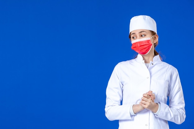 Vue de face de la jeune infirmière stressée en costume médical avec masque rouge sur le bleu