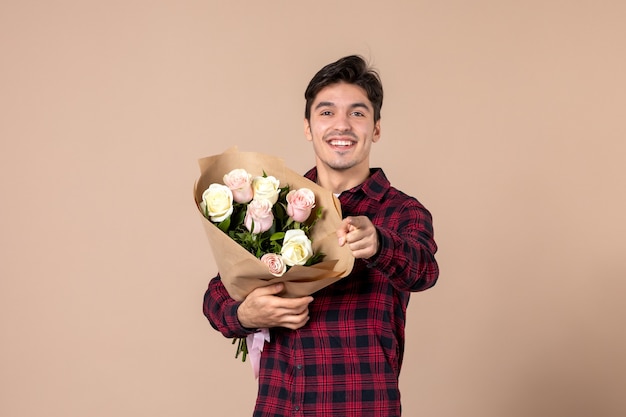 Vue de face jeune mâle tenant de belles fleurs sur mur marron
