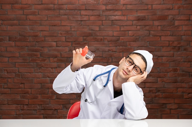 Vue de face jeune médecin en costume médical blanc tenant une petite fiole vide