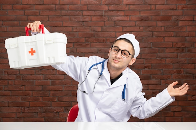 Photo vue de face jeune médecin en costume médical blanc avec trousse de premiers soins